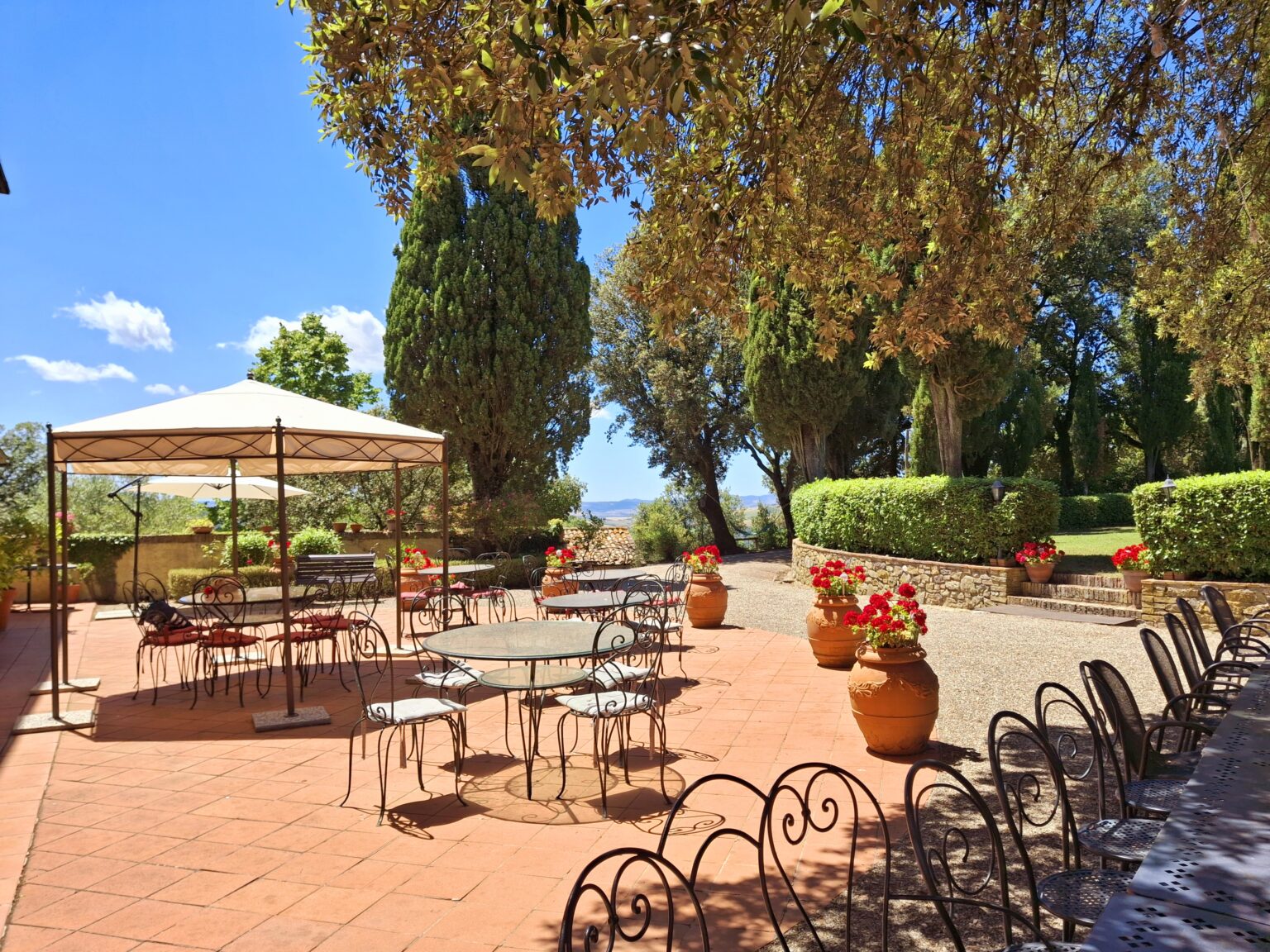 Outdoor garden patio with tables and chairs under a canopy, surrounded by lush greenery and blooming flowers, ideal for dining and relaxation. | Only on SopranoVillas