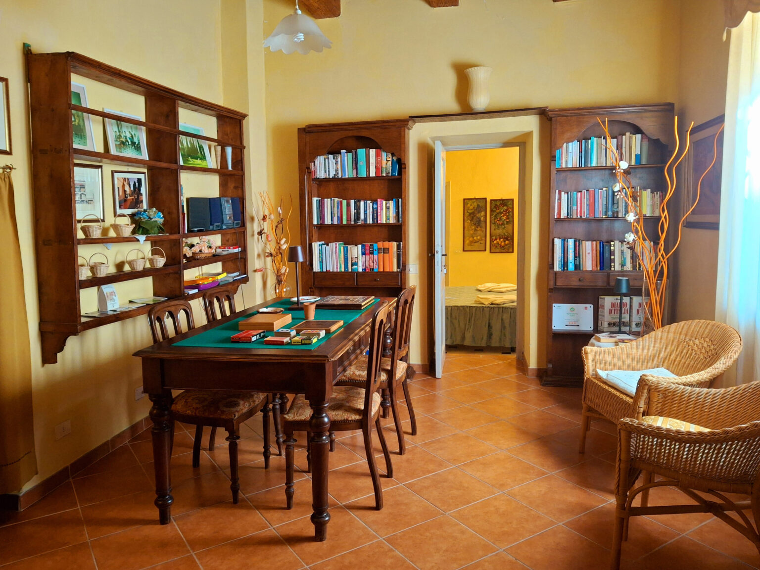 Cozy game room featuring a wooden table with chairs, bookshelves filled with books, and a doorway leading to a bedroom. Natural light fills the space, highlighting the warm colors and inviting atmosphere. | Only on SopranoVillas