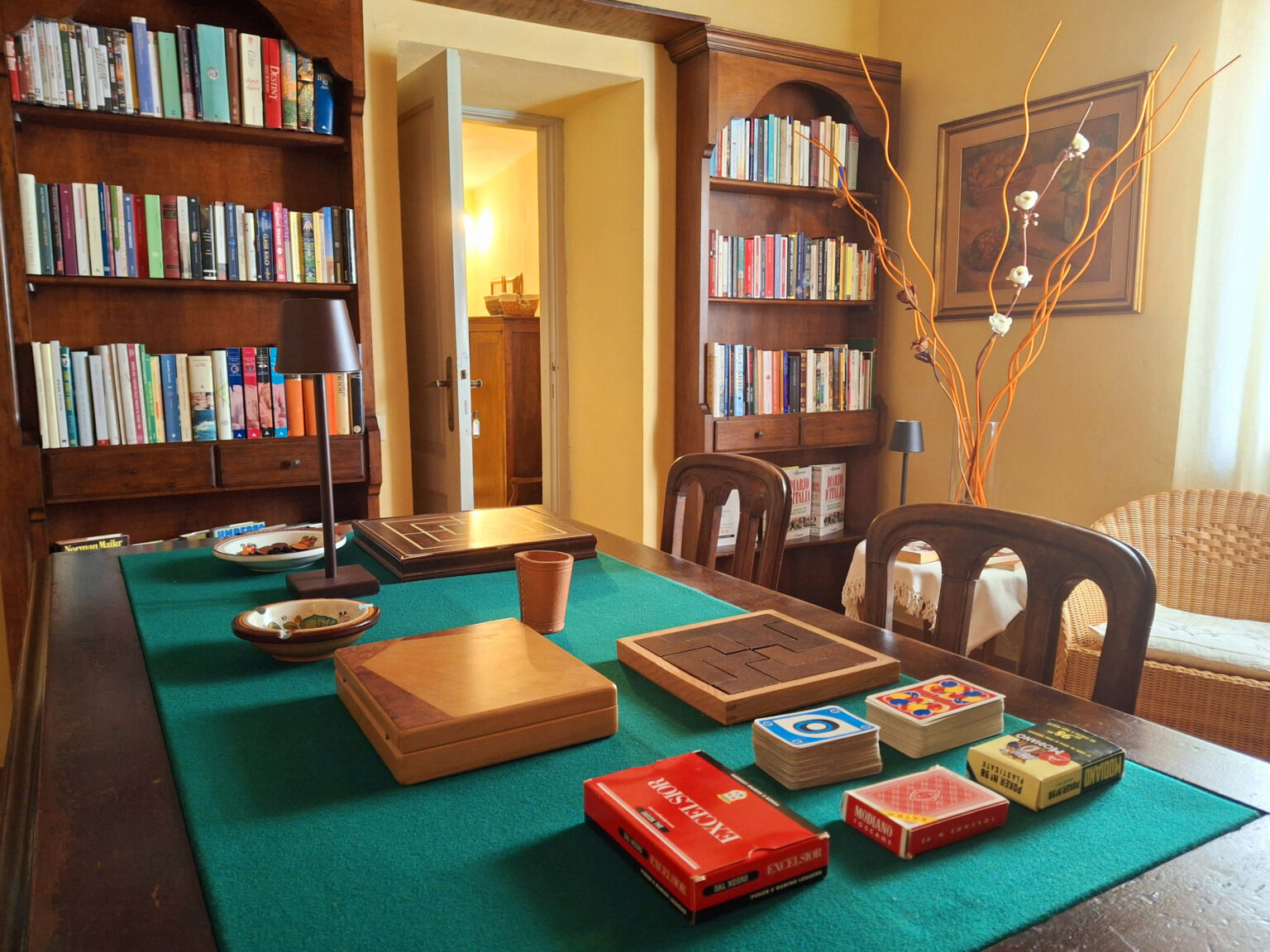 Cozy reading room featuring a wooden table with various board games and playing cards, surrounded by bookshelves filled with colorful books, creating an inviting atmosphere for leisure and entertainment. | Only on SopranoVillas