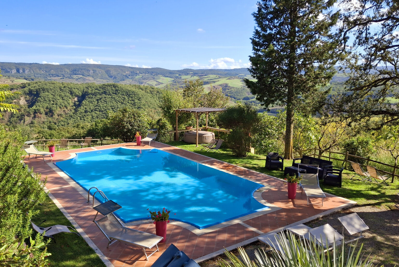 Scenic outdoor swimming pool surrounded by lush greenery and mountains, featuring lounge chairs and a pergola in a tranquil setting. Ideal for relaxation and leisure activities. | Only on SopranoVillas