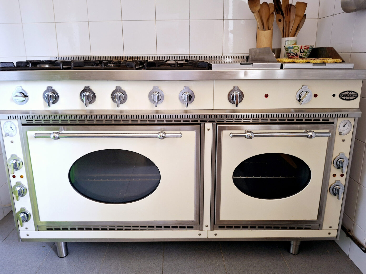 Professional kitchen range with multiple burners, dual ovens, and stainless steel accents, set against a tiled wall. Ideal for culinary enthusiasts and chefs. | Only on SopranoVillas