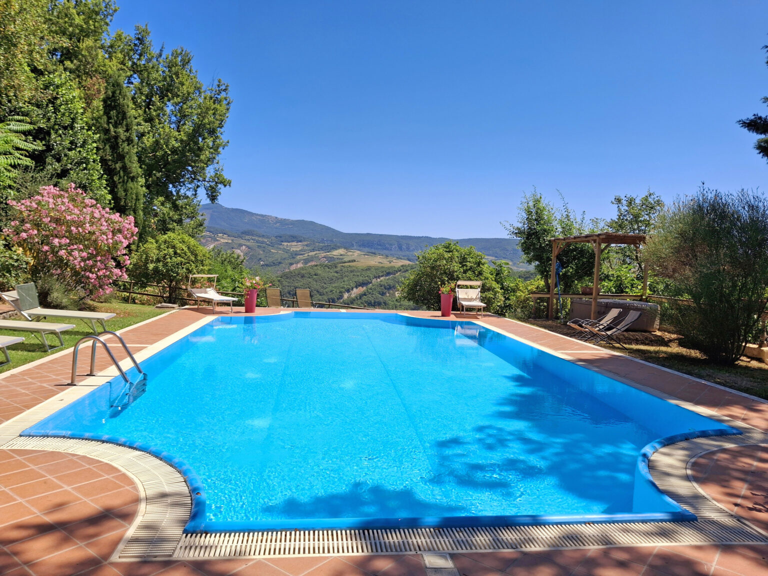 Scenic outdoor swimming pool surrounded by lush greenery and mountains, ideal for relaxation and leisure in a sunny setting. | Only on SopranoVillas
