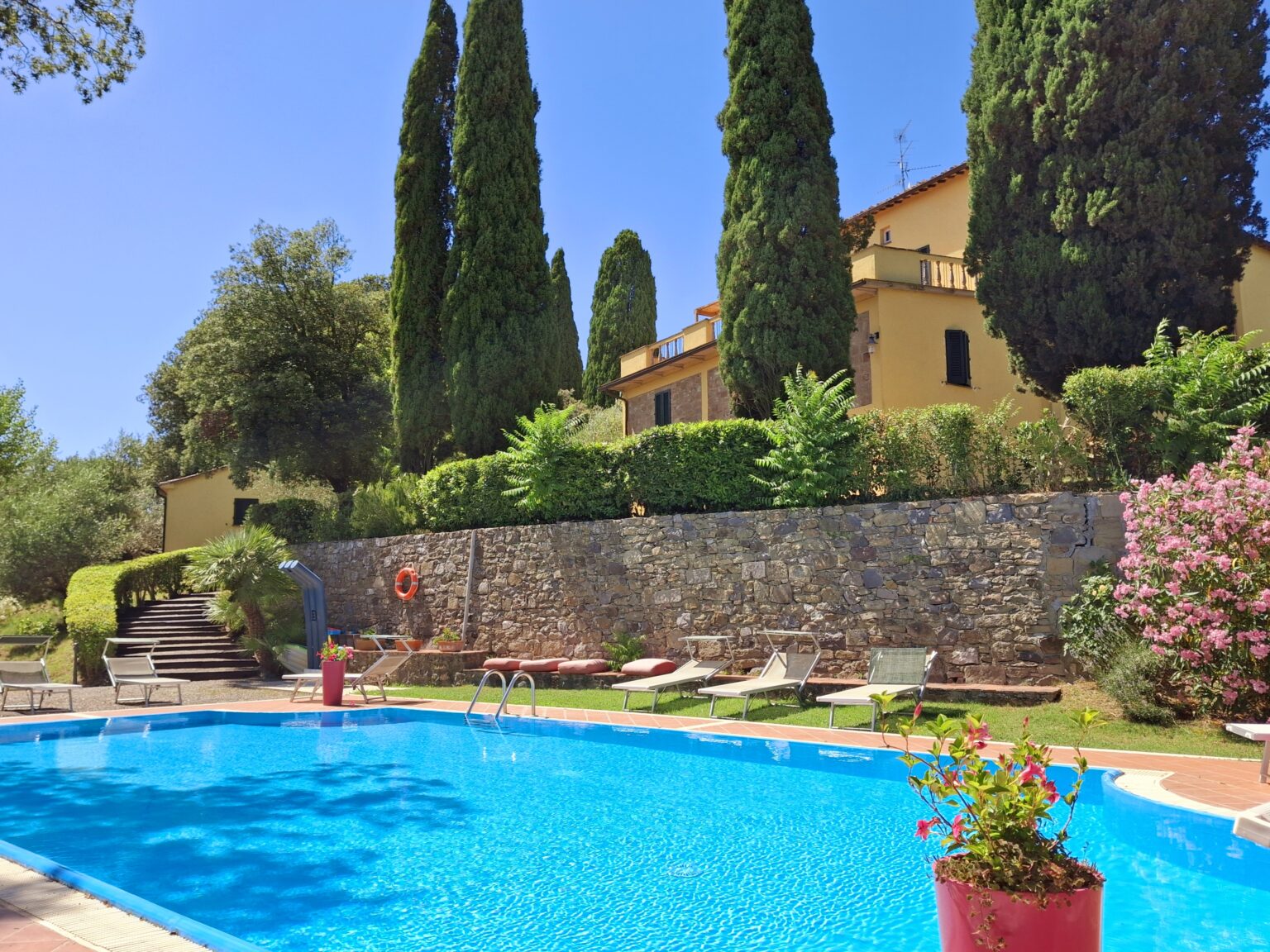 Scenic view of a luxury villa with a swimming pool surrounded by lush greenery and tall cypress trees, offering a relaxing outdoor space in sunny weather. | Only on SopranoVillas