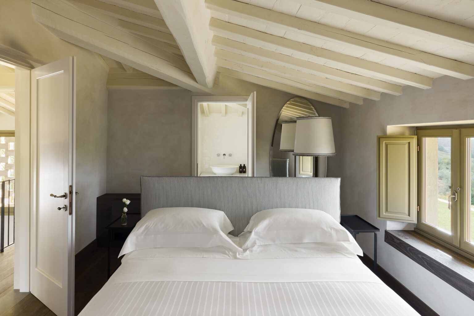Cozy bedroom featuring a plush bed with white linens, elegant wooden beams, and soft natural light from windows. The room includes stylish decor, a bedside lamp, and a minimalist design for a serene atmosphere. | Only on SopranoVillas