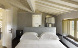 Cozy bedroom featuring a plush bed with white linens, elegant wooden beams, and soft natural light from windows. The room includes stylish decor, a bedside lamp, and a minimalist design for a serene atmosphere.