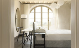 Modern bedroom interior featuring a large arched window, minimalist furniture including a bed, desk, and chair, soft natural light, and decorative pendant lamps for a cozy ambiance.