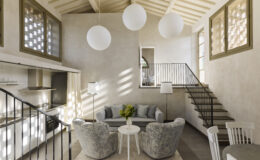 Modern living room with a cozy seating area featuring plush gray chairs and a white coffee table, illuminated by three spherical pendant lights. The open layout includes a staircase leading to a second floor, with large windows allowing natural light to fill the space. The neutral color palette creates a serene atmosphere, ideal for contemporary home design.