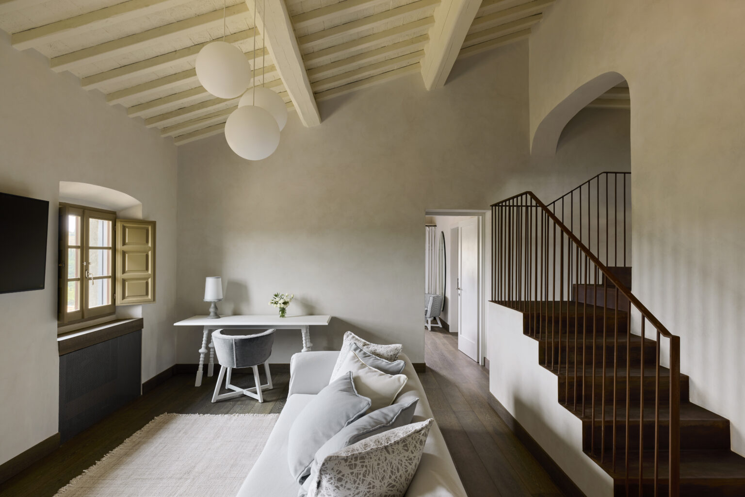 Modern living room with rustic decor featuring a cozy sofa, a stylish dining table, and elegant pendant lights, complemented by wooden flooring and a staircase leading to an upper level. | Only on SopranoVillas