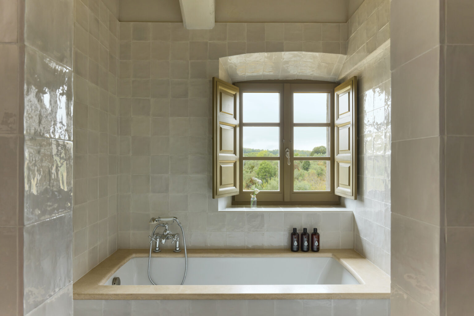 Modern bathroom featuring a bathtub with a natural stone countertop, open wooden windows providing a scenic view, and neatly arranged toiletries on the ledge. | Only on SopranoVillas