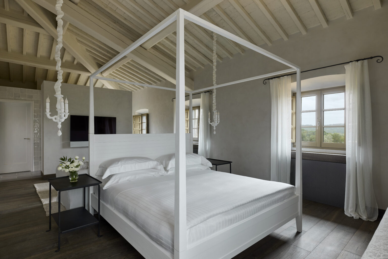 Modern bedroom featuring a white four-poster bed, minimalist decor, and large windows with scenic views, ideal for relaxation and comfort. | Only on SopranoVillas