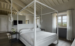 Modern bedroom featuring a white four-poster bed, minimalist decor, and large windows with scenic views, ideal for relaxation and comfort.