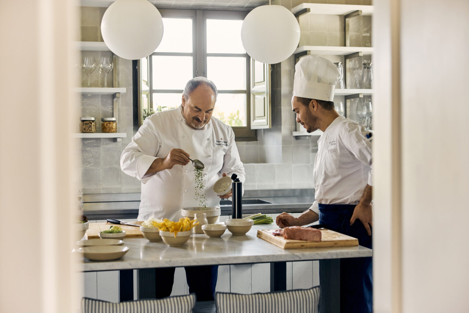 Two chefs preparing a gourmet dish in a modern kitchen, featuring fresh ingredients on a counter and stylish decor. | Only on SopranoVillas