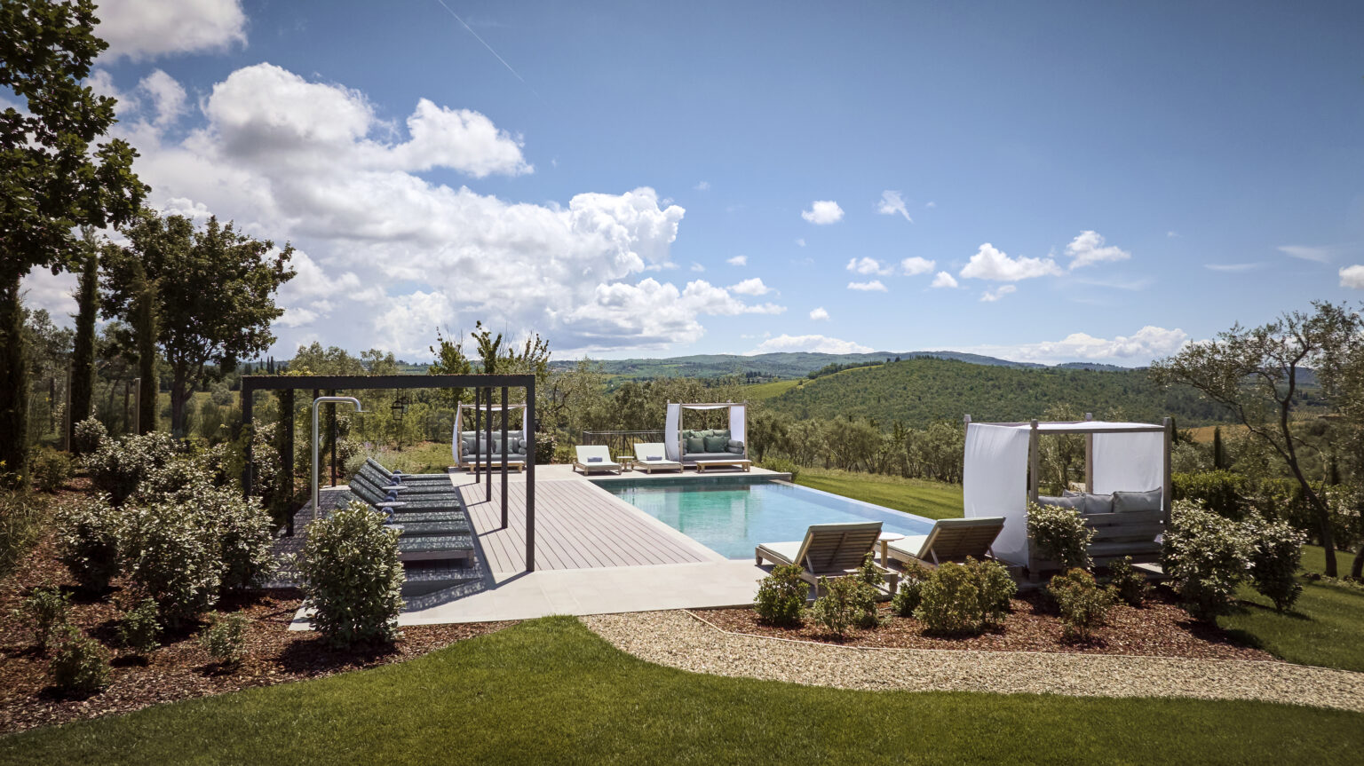 Luxurious outdoor pool area with lounge chairs, cabanas, and scenic mountain views, surrounded by lush greenery and a clear blue sky. Ideal for relaxation and leisure in a serene setting. | Only on SopranoVillas