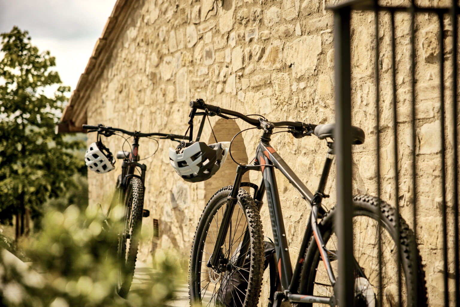 Two mountain bikes with helmets hanging on handlebars, positioned against a rustic stone wall, surrounded by greenery. | Only on SopranoVillas