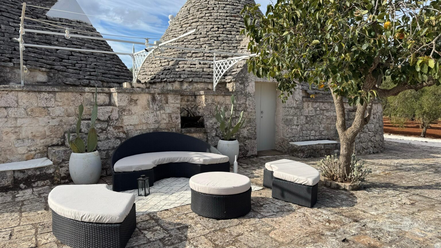 Outdoor seating area featuring modern black and white furniture, surrounded by traditional stone trulli architecture and greenery. Ideal for relaxation in a scenic setting. | Only on SopranoVillas