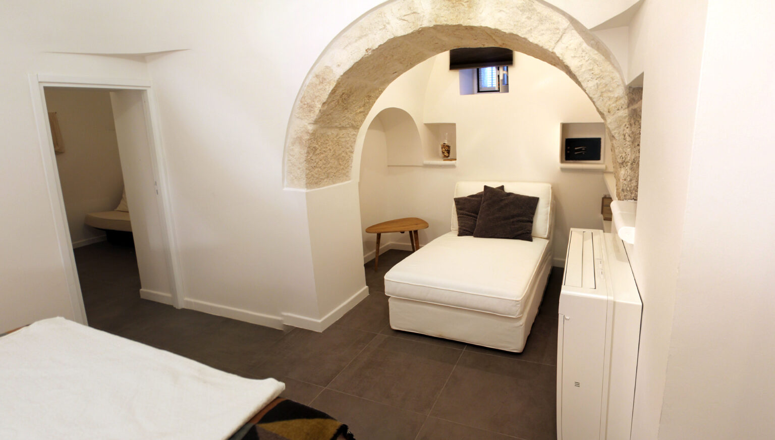 Cozy interior of a modern bedroom featuring an arched stone ceiling, a single bed with decorative pillows, and minimalist decor, showcasing a blend of contemporary and traditional design elements. | Only on SopranoVillas