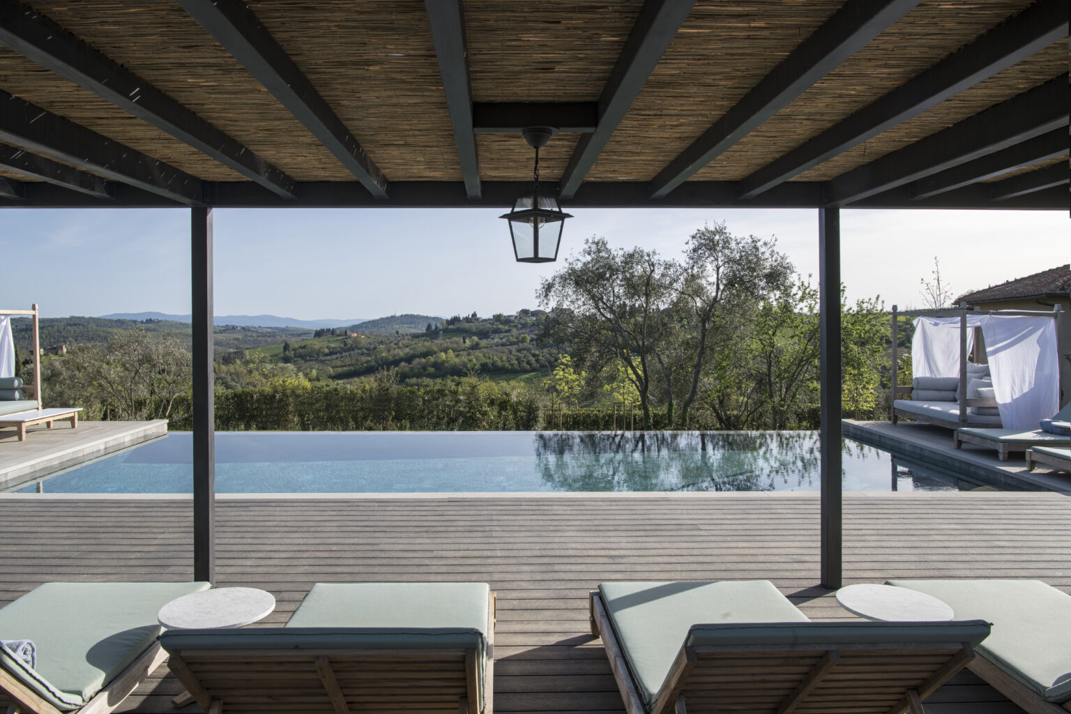Luxurious outdoor pool area with sun loungers, featuring a stunning view of rolling hills and lush greenery, under a wooden pergola. Ideal for relaxation and enjoying nature. | Only on SopranoVillas