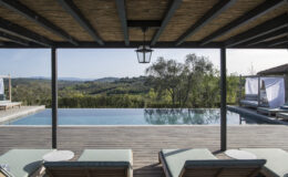Luxurious outdoor pool area with sun loungers, featuring a stunning view of rolling hills and lush greenery, under a wooden pergola. Ideal for relaxation and enjoying nature.