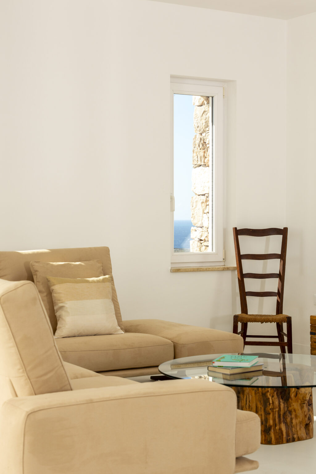 Cozy living room featuring a beige sofa with decorative pillows, a wooden chair, and a bright window showcasing a scenic view. Ideal for interior design inspiration. | Only on SopranoVillas