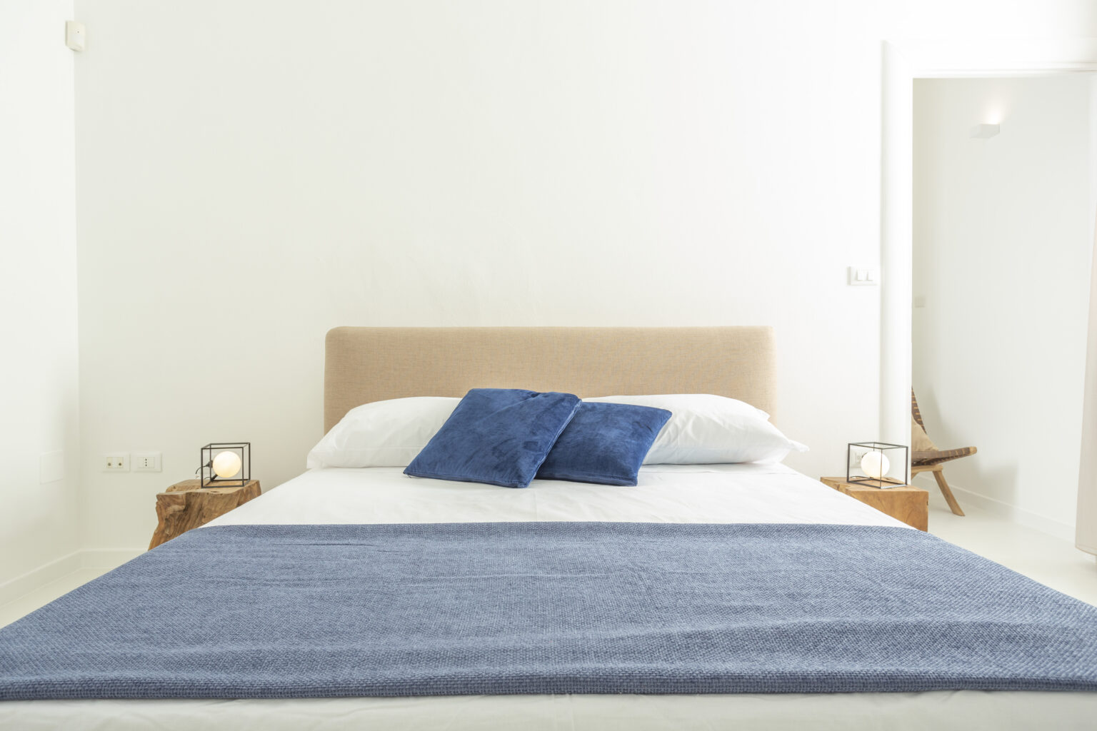 Modern bedroom interior featuring a neatly made bed with blue pillows and a cozy blanket, complemented by minimalist decor and soft lighting. | Only on SopranoVillas