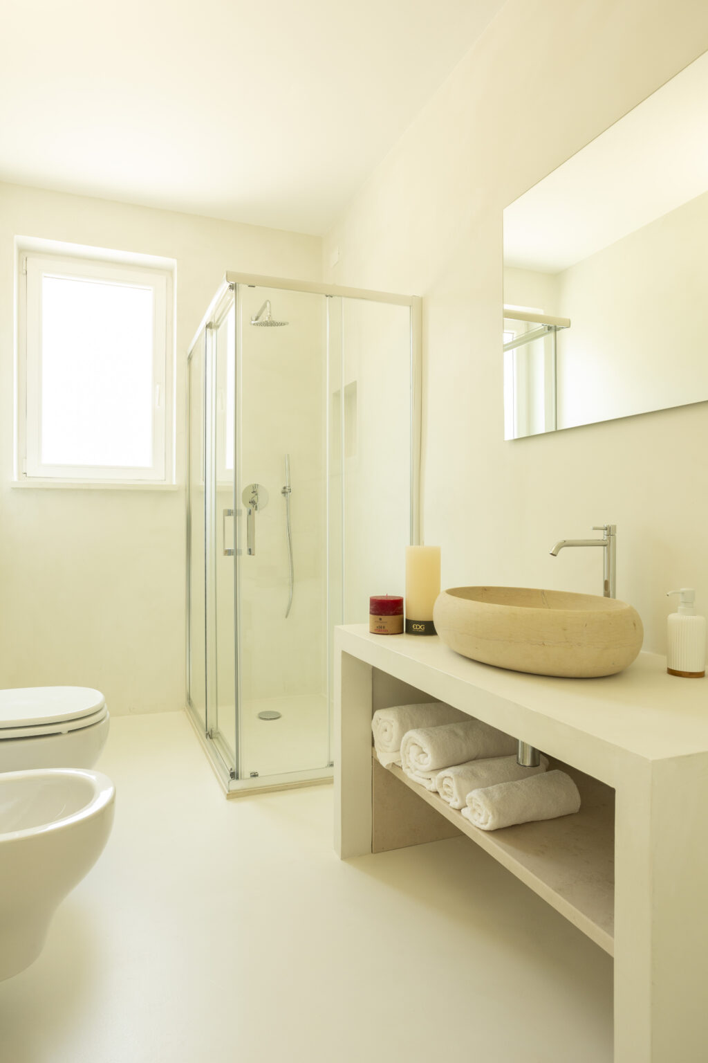 Modern bathroom interior featuring a glass shower, minimalist decor, a wooden sink bowl, and neatly arranged towels. Natural light illuminates the space, enhancing the clean and airy atmosphere. | Only on SopranoVillas