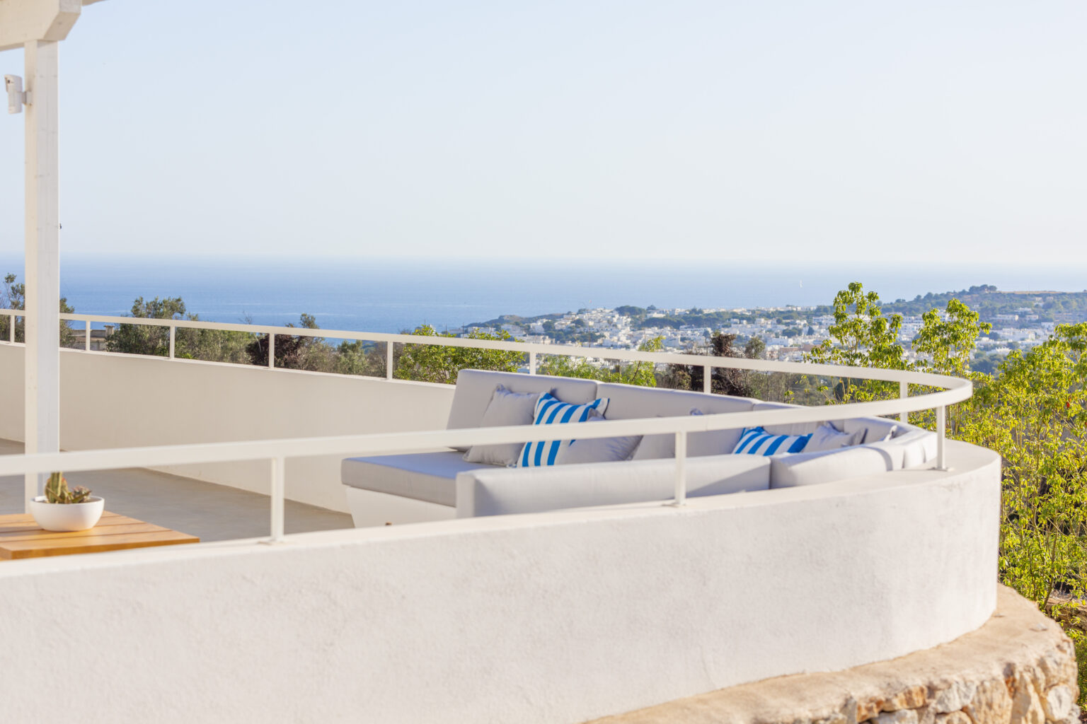 Modern outdoor terrace with a comfortable seating area offering a panoramic view of the ocean and surrounding landscape, featuring stylish cushions in blue and white. | Only on SopranoVillas