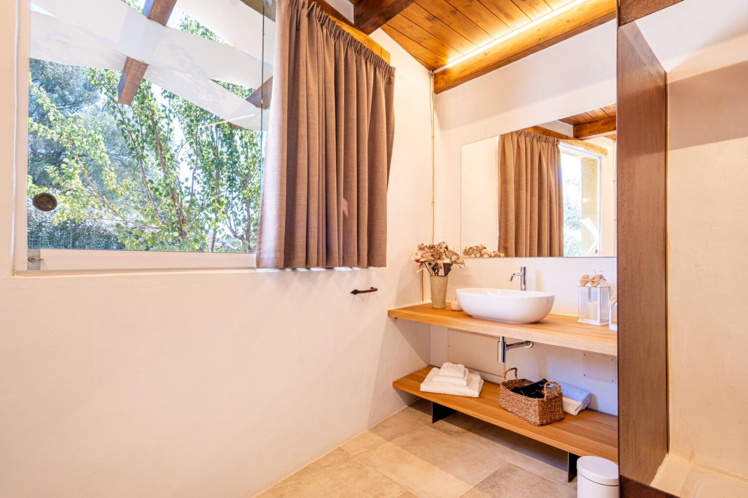Modern bathroom interior featuring a wooden countertop with a stylish sink, natural light from a window, and elegant curtains, creating a serene and inviting atmosphere. | Only on SopranoVillas