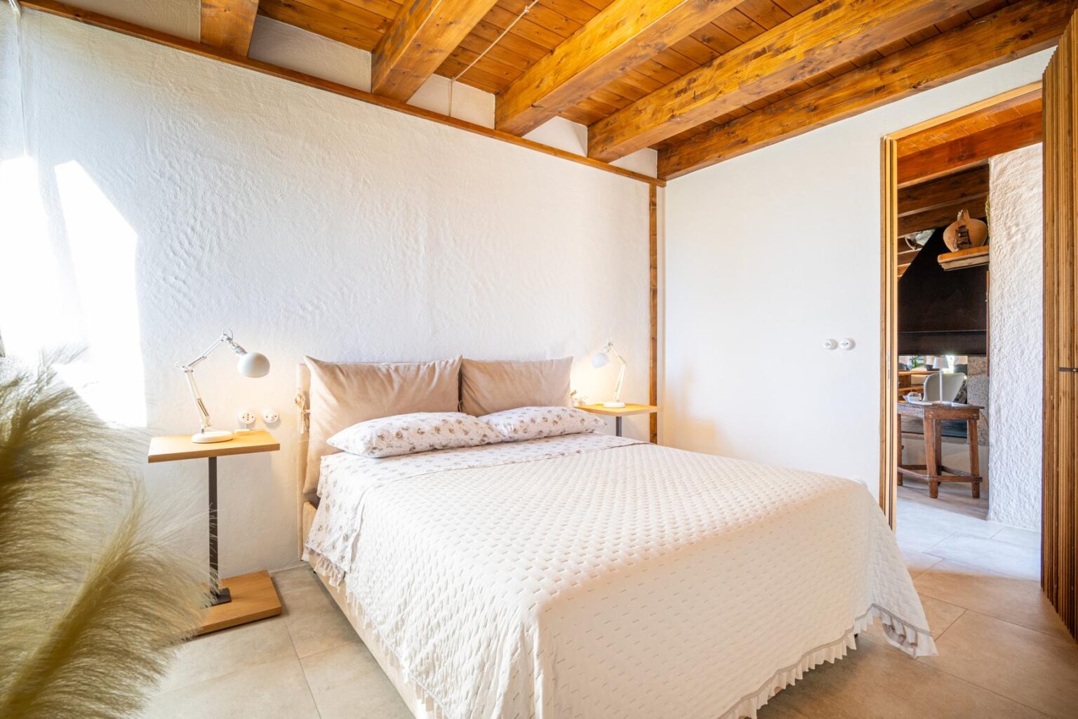 Cozy bedroom featuring a queen-sized bed with neutral bedding, wooden ceiling beams, and bedside lamps, creating a warm and inviting atmosphere. | Only on SopranoVillas