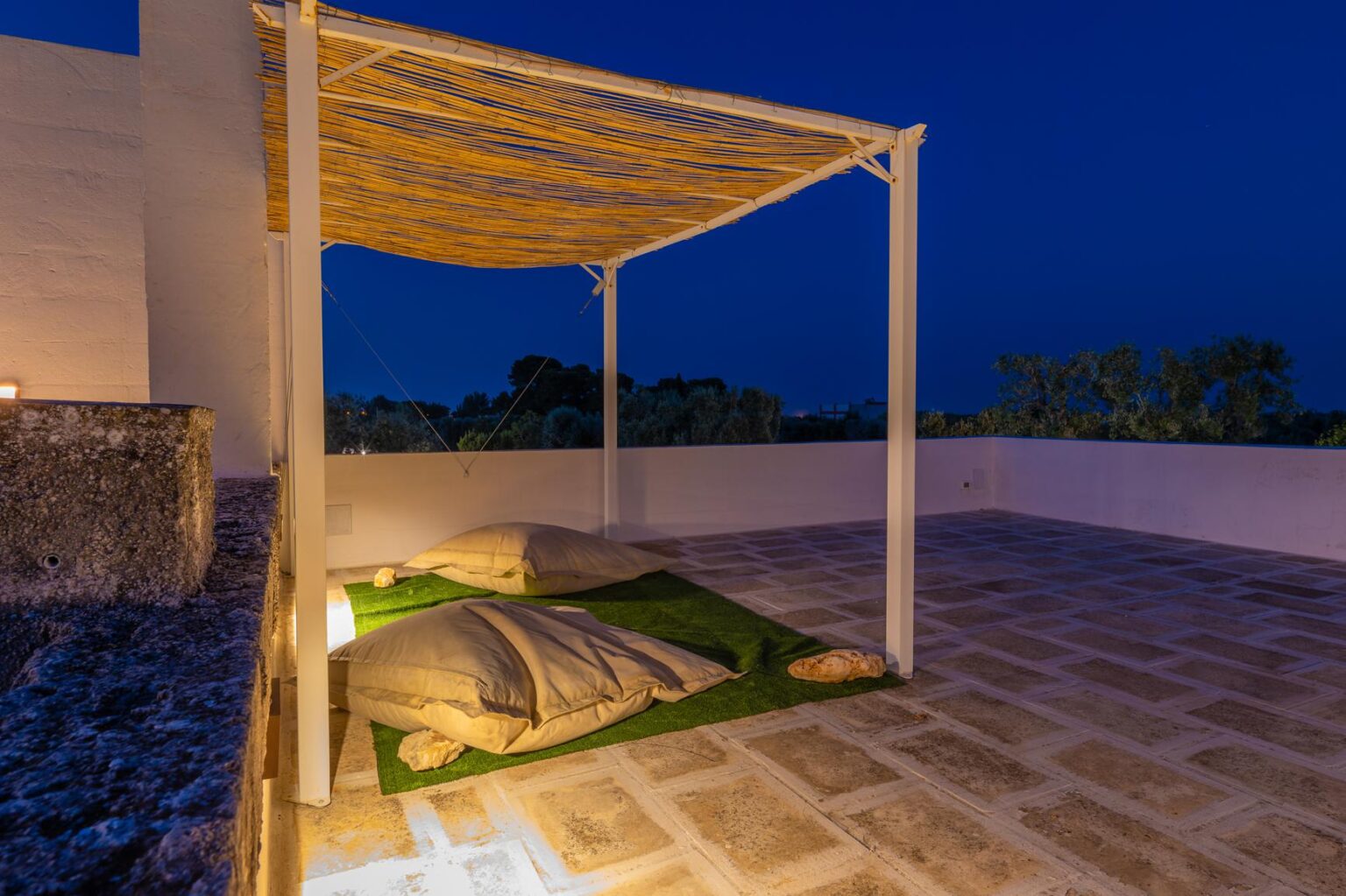 Cozy outdoor seating area with a canopy, illuminated at night, featuring soft cushions on a grassy surface and a serene atmosphere. | Only on SopranoVillas