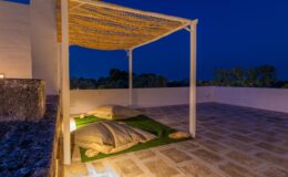 Cozy outdoor seating area with a canopy, illuminated at night, featuring soft cushions on a grassy surface and a serene atmosphere.
