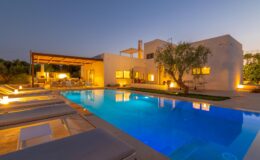 Modern luxury villa with a swimming pool, illuminated at dusk, surrounded by lush greenery and outdoor seating areas. Ideal for relaxation and entertainment.