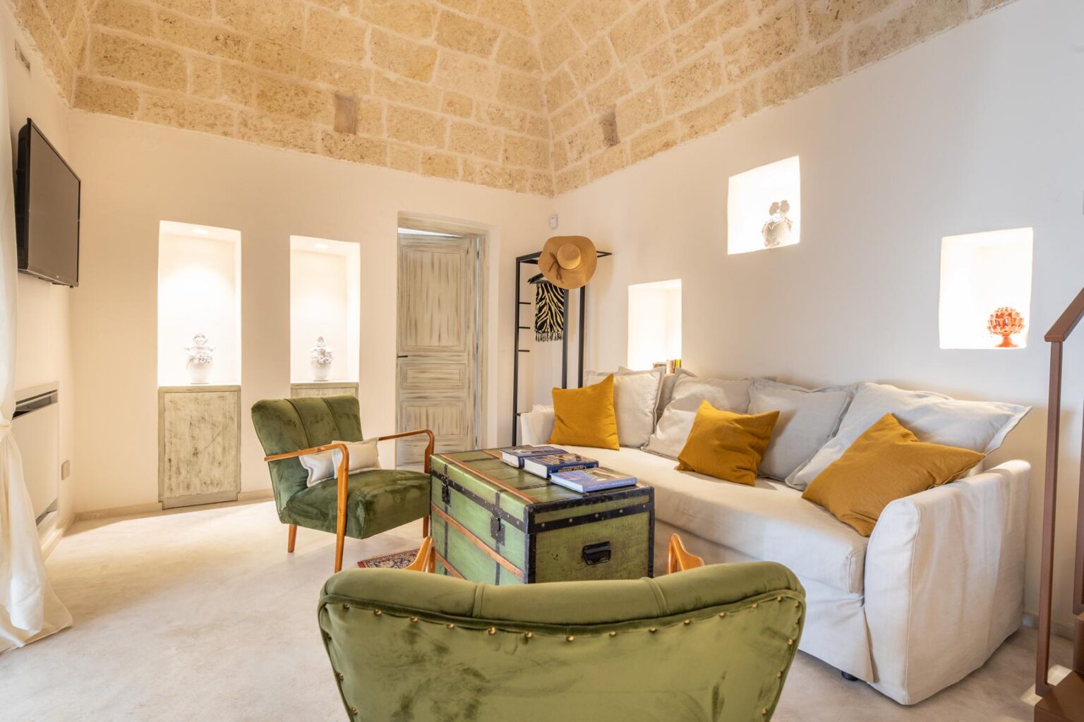 Cozy living room featuring a white sofa with colorful cushions, a green armchair, a wooden coffee table, and natural stone walls, creating a warm and inviting atmosphere. | Only on SopranoVillas