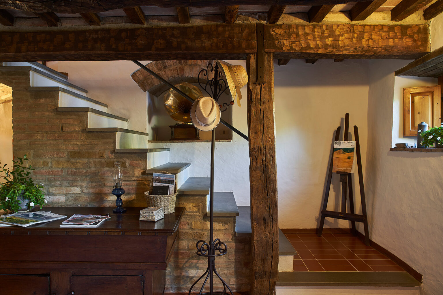 Rustic interior of a cozy home featuring wooden beams, a staircase, and a kitchen area with a vintage hat stand and potted plants, creating a warm and inviting atmosphere. | Only on SopranoVillas