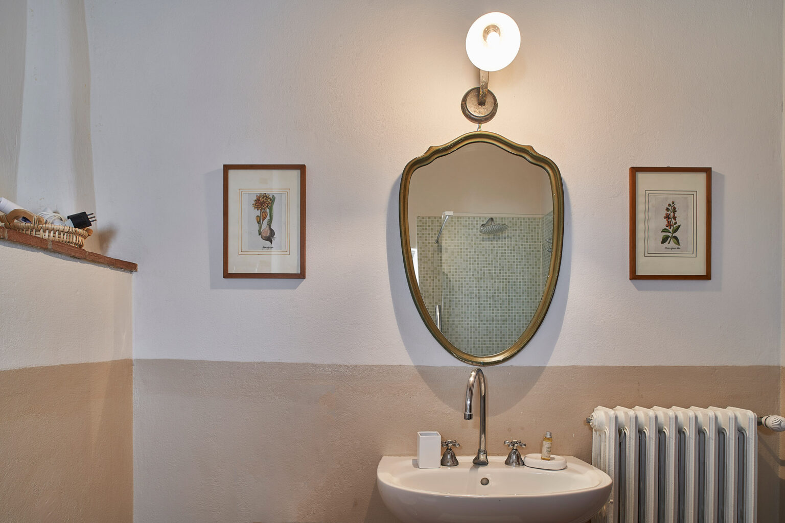 Elegant bathroom interior featuring a vintage mirror above a modern sink, framed artwork on the walls, and a classic radiator, providing a blend of style and functionality. | Only on SopranoVillas
