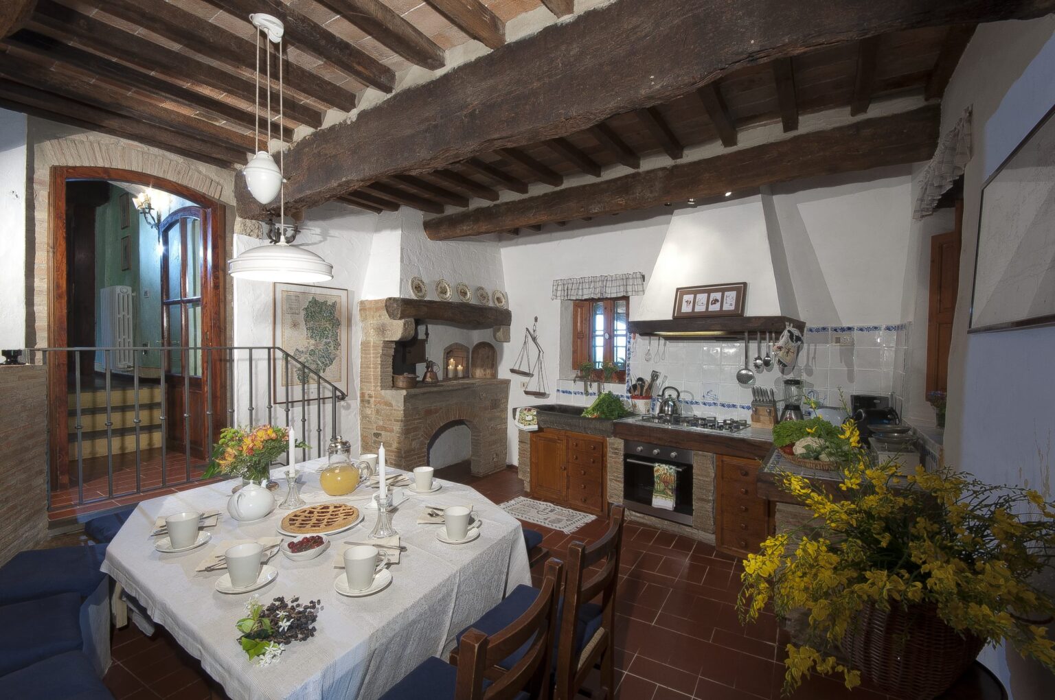 Rustic kitchen interior featuring wooden beams, a dining table set with dishes, and a cozy fireplace. The space showcases a blend of traditional and modern elements, with natural light illuminating the room. | Only on SopranoVillas