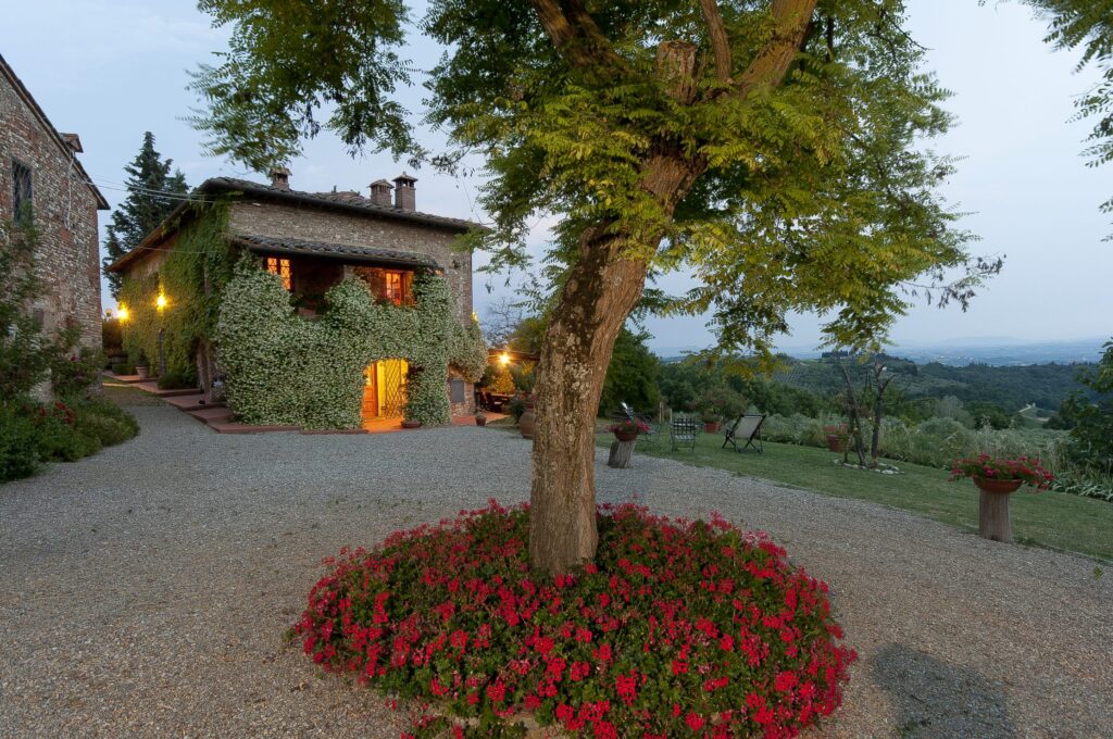 Charming rustic villa surrounded by lush greenery and vibrant flower beds, set against a scenic landscape during twilight. | Only on SopranoVillas