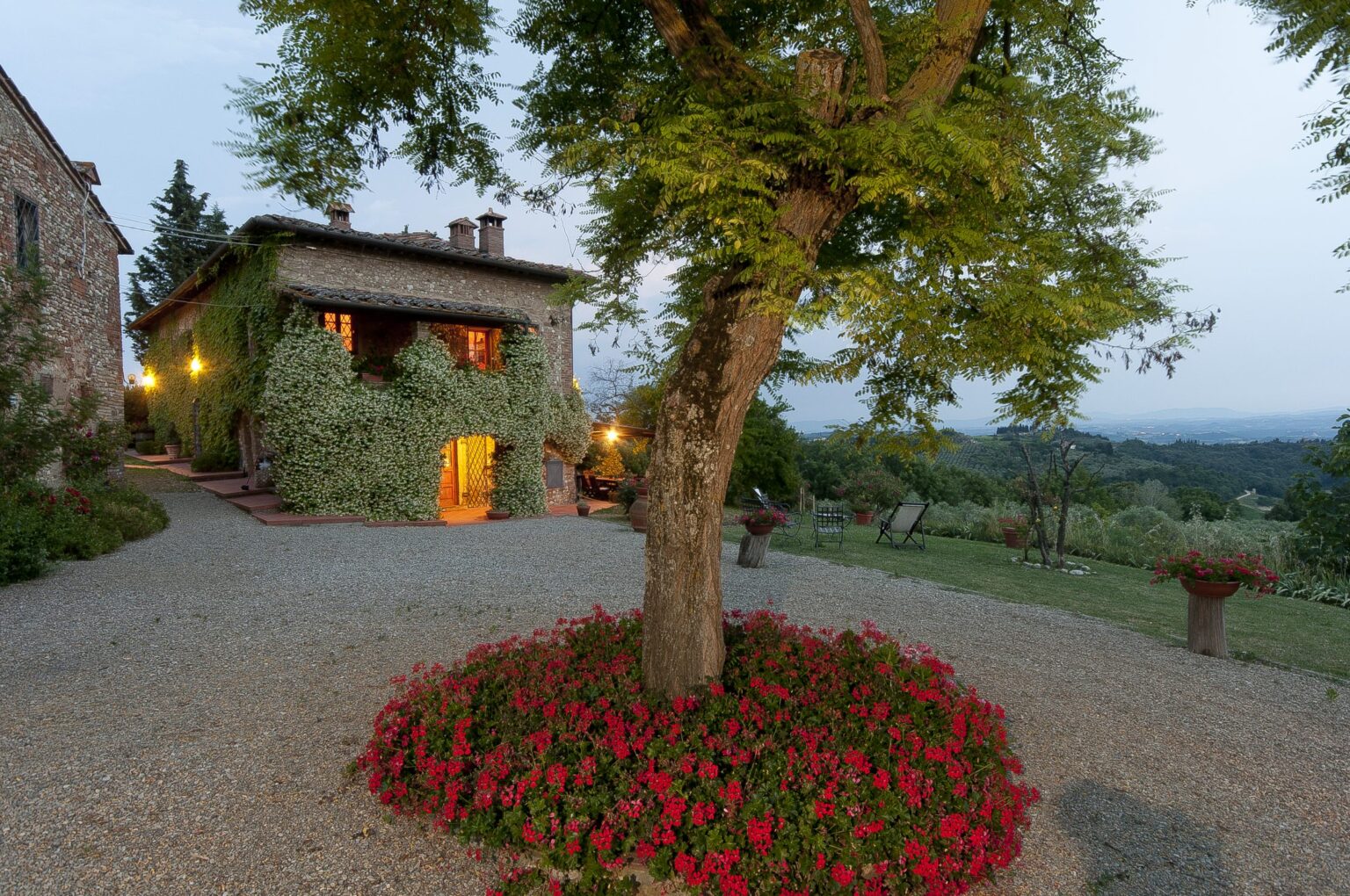 Charming rustic villa surrounded by lush greenery and vibrant flower beds, set against a scenic landscape during twilight. | Only on SopranoVillas