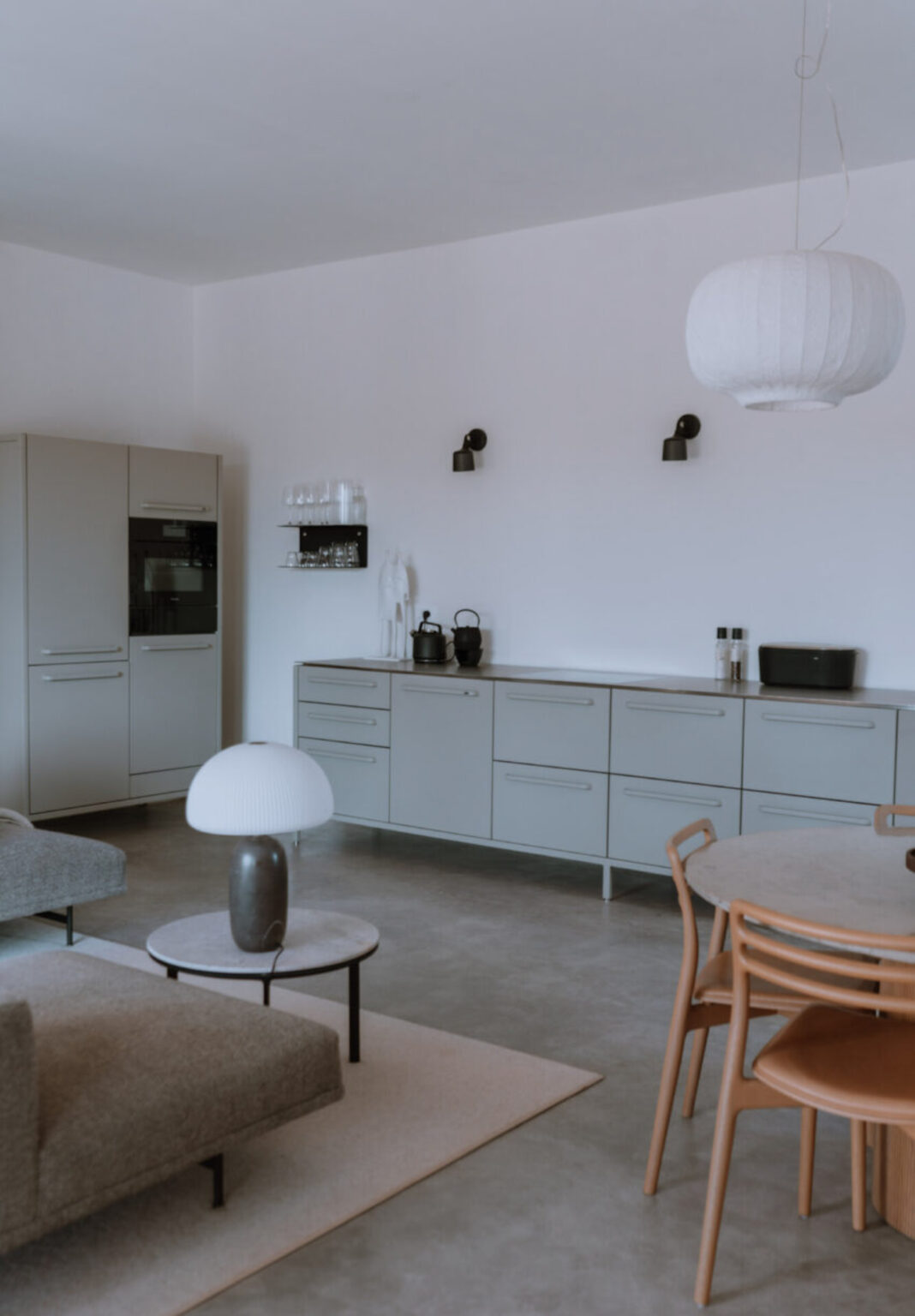 Modern kitchen interior featuring sleek gray cabinetry, a stainless steel refrigerator, and minimalist decor. The space includes a stylish dining table and contemporary lighting, creating a functional and aesthetic environment. | Only on SopranoVillas