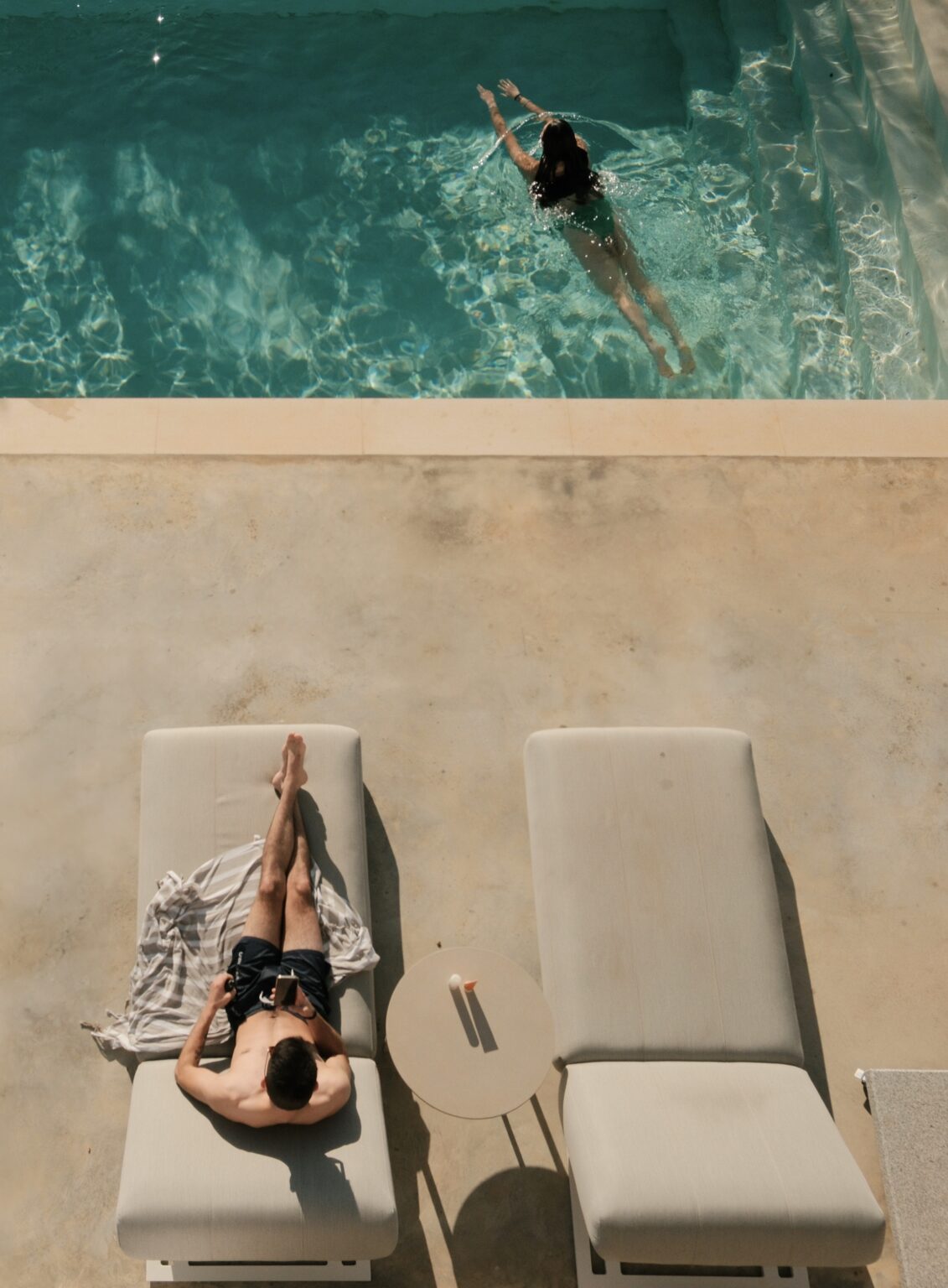 Aerial view of a person relaxing on a sun lounger beside a turquoise swimming pool, showcasing a serene outdoor leisure setting. | Only on SopranoVillas