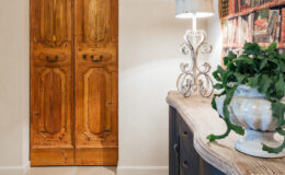 Rustic wooden double doors in a stylish entryway, accompanied by an elegant lamp and a decorative plant in a ceramic pot, showcasing a blend of modern and traditional design elements.