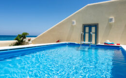Luxurious outdoor swimming pool with crystal-clear water, surrounded by a serene coastal landscape and a modern architectural backdrop. Perfect for relaxation and enjoying sunny weather.