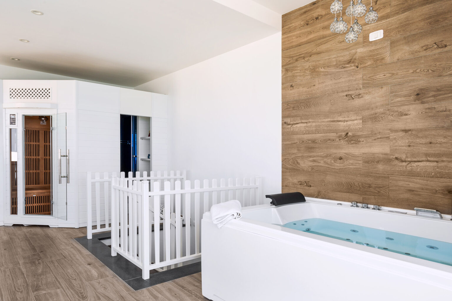 Modern spa interior featuring a white hot tub, a wooden accent wall, and a sauna room, designed for relaxation and wellness. | Only on SopranoVillas