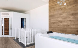 Modern spa interior featuring a white hot tub, a wooden accent wall, and a sauna room, designed for relaxation and wellness.