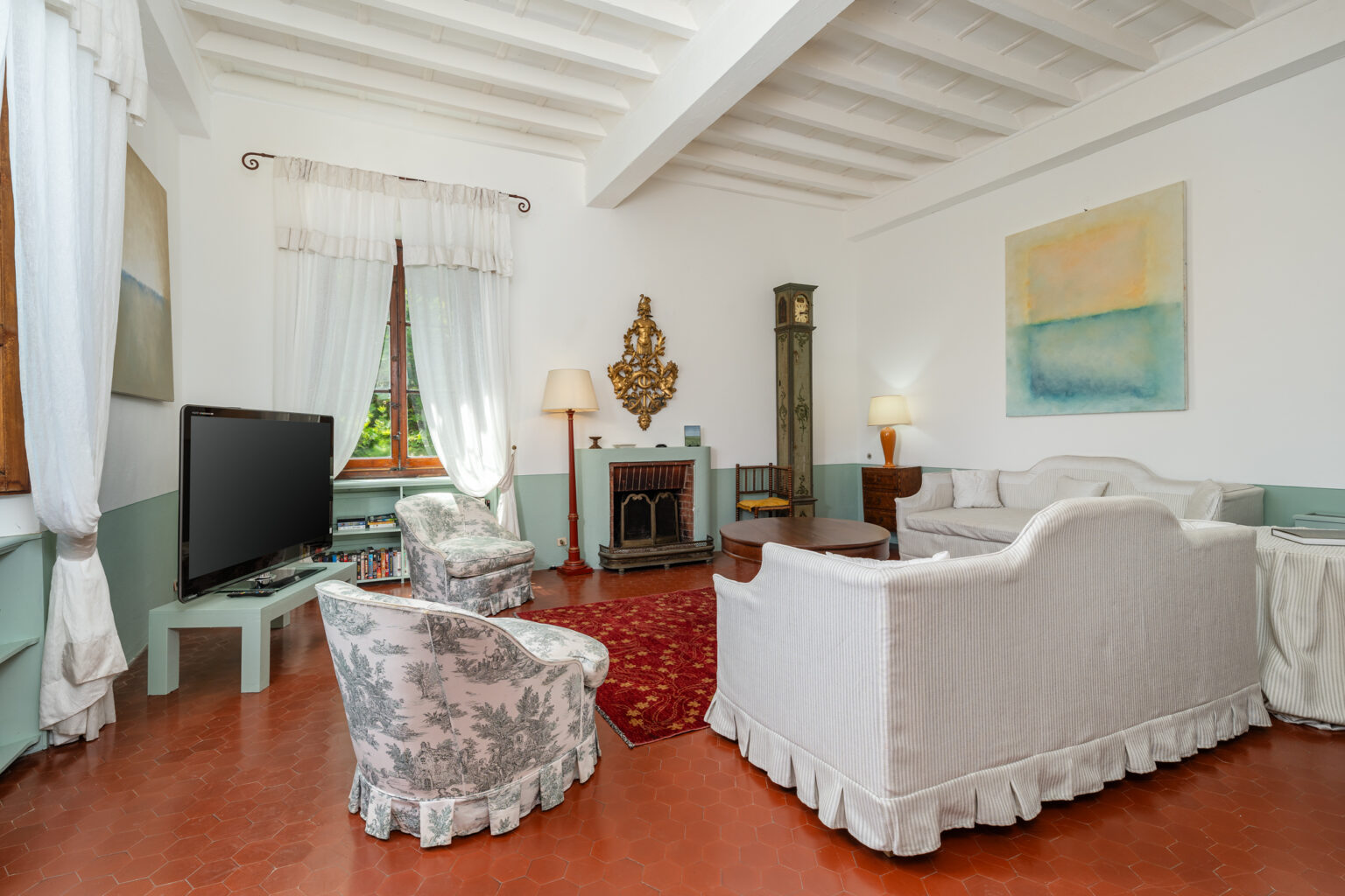 Cozy living room with white furniture, wooden beams, and a vintage clock, featuring a large TV and artistic decor, perfect for relaxation and entertainment. | Only on SopranoVillas