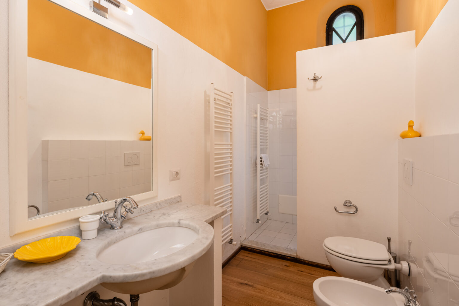 Modern bathroom featuring a spacious shower, marble vanity with sink, and stylish yellow accents on the walls. The design includes a large mirror and a window for natural light. | Only on SopranoVillas