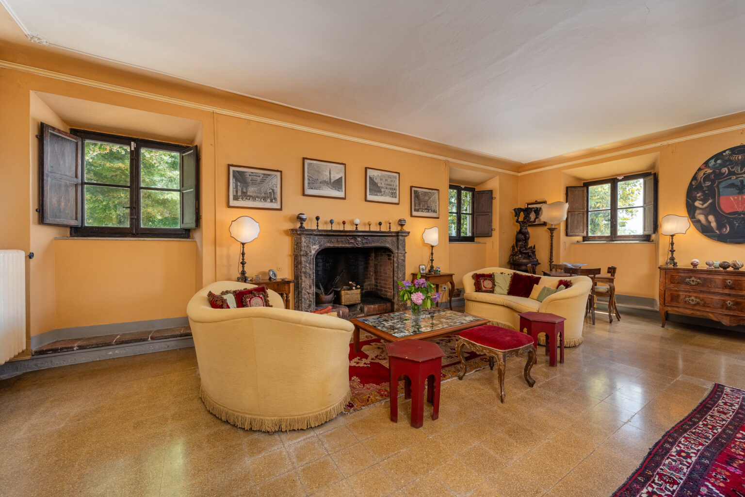 Cozy living room featuring yellow walls, a fireplace, and elegant seating arrangements with a vintage feel. Natural light streams in through windows, highlighting framed artwork and decorative furnishings. Ideal for relaxation and social gatherings. | Only on SopranoVillas
