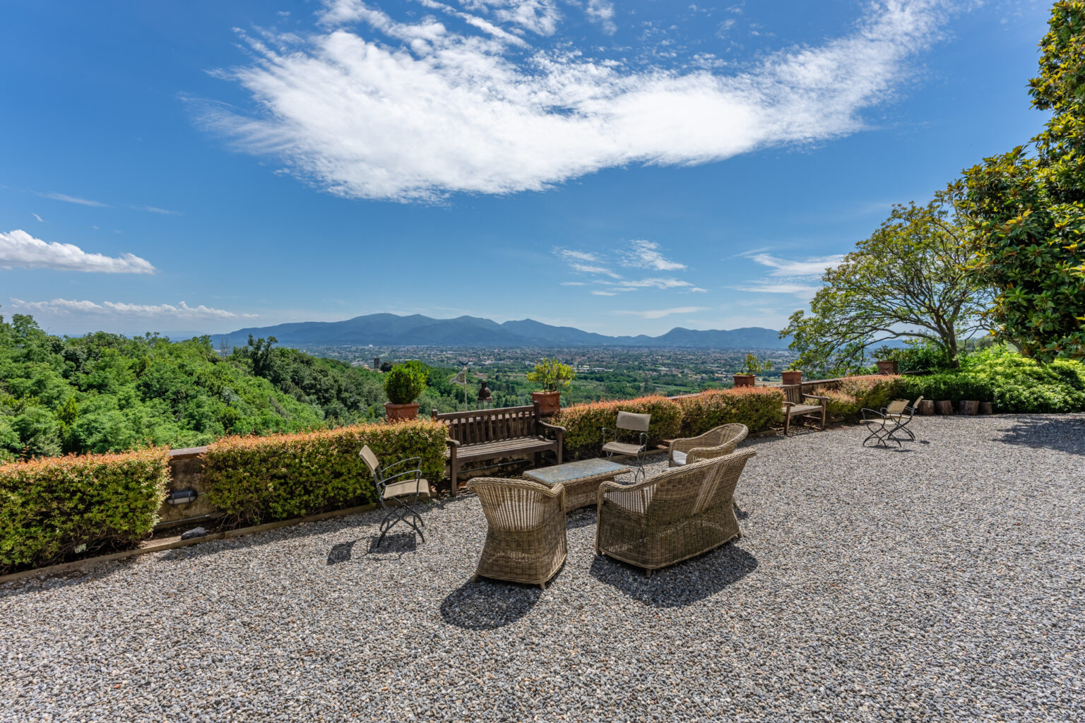 Scenic outdoor terrace with comfortable wicker furniture overlooking lush green hills and mountains under a clear blue sky. | Only on SopranoVillas