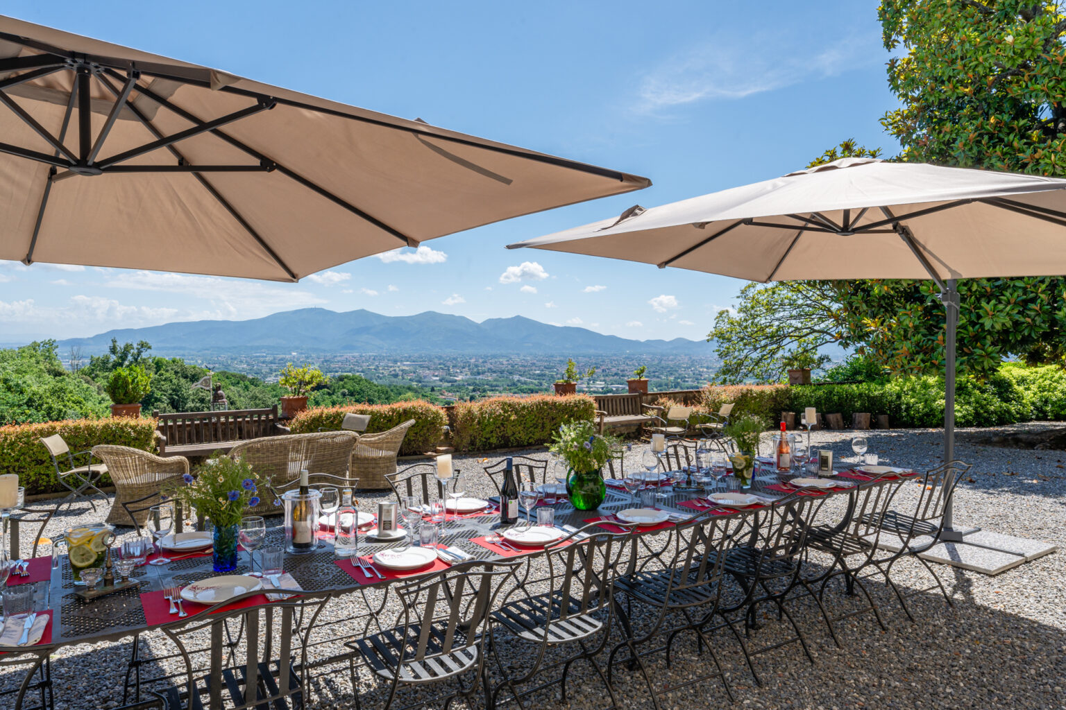 Outdoor dining setup with a long table under large umbrellas, featuring scenic mountain views and lush greenery, ideal for events and gatherings. | Only on SopranoVillas