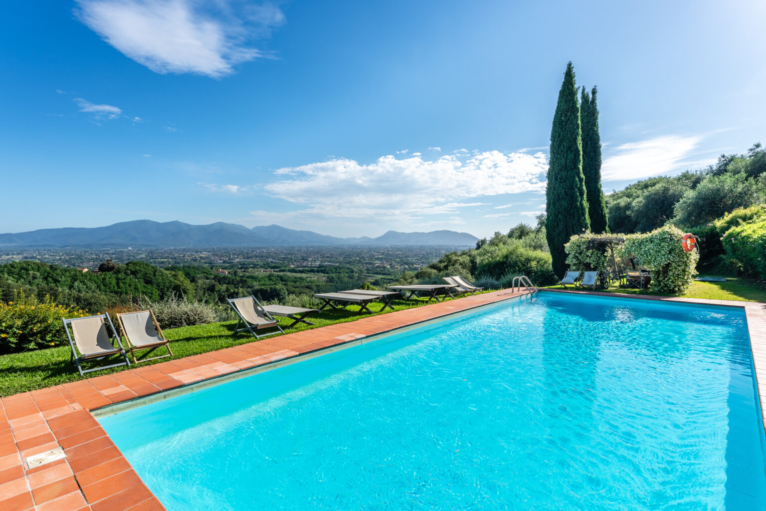 Scenic outdoor swimming pool surrounded by lush greenery and sun loungers, with stunning mountain views and a clear blue sky. Ideal for relaxation and leisure in a tranquil setting. | Only on SopranoVillas