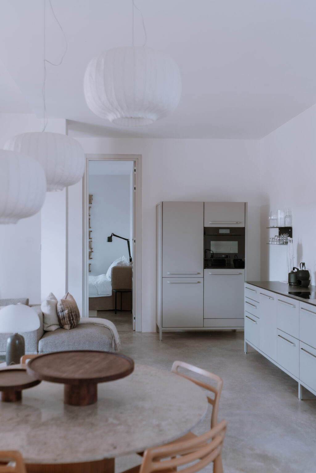 Modern kitchen interior featuring a sleek refrigerator, minimalist cabinetry, and a cozy living area visible through an open doorway. Soft lighting and neutral tones create a warm and inviting atmosphere. | Only on SopranoVillas